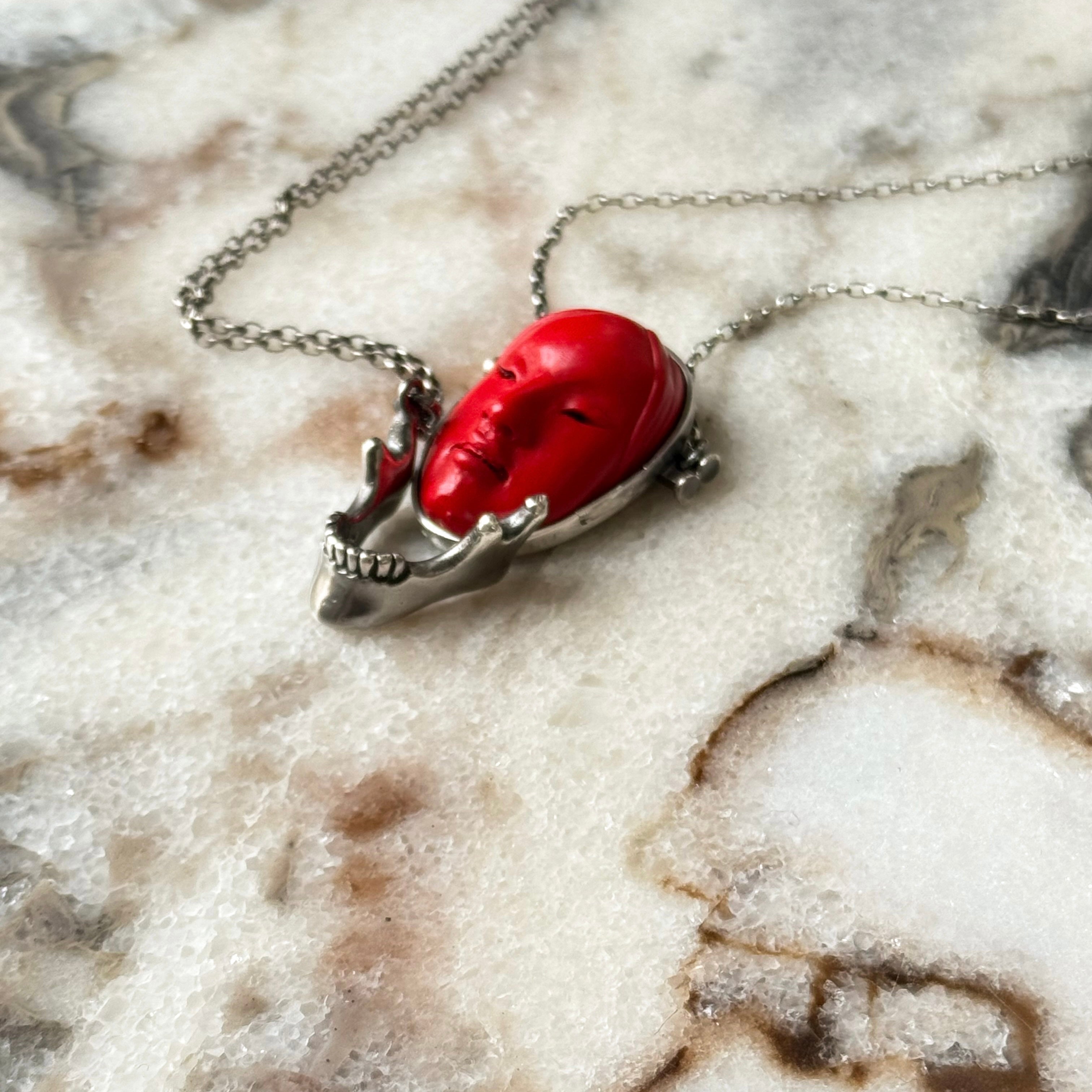 Silver Skull Jaw pendant and Red Noh Mask pendant by Macabre Gadgets on a marble surface