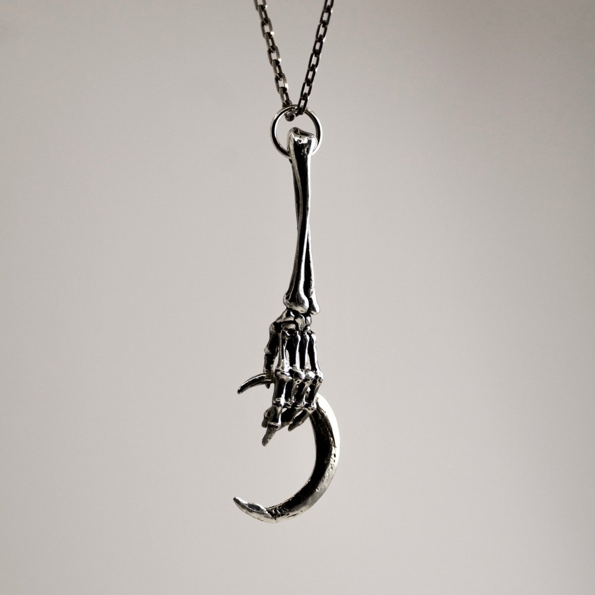Silver Skeleton Hand & Crescent Moon pendant - silver charm against neutral background