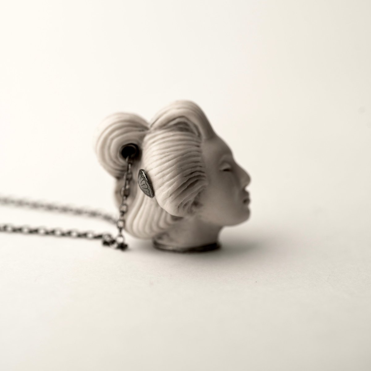 She pendant, white variant, placed on a white surface, side view - shows us a hair decoration and side profile of a woman's head
