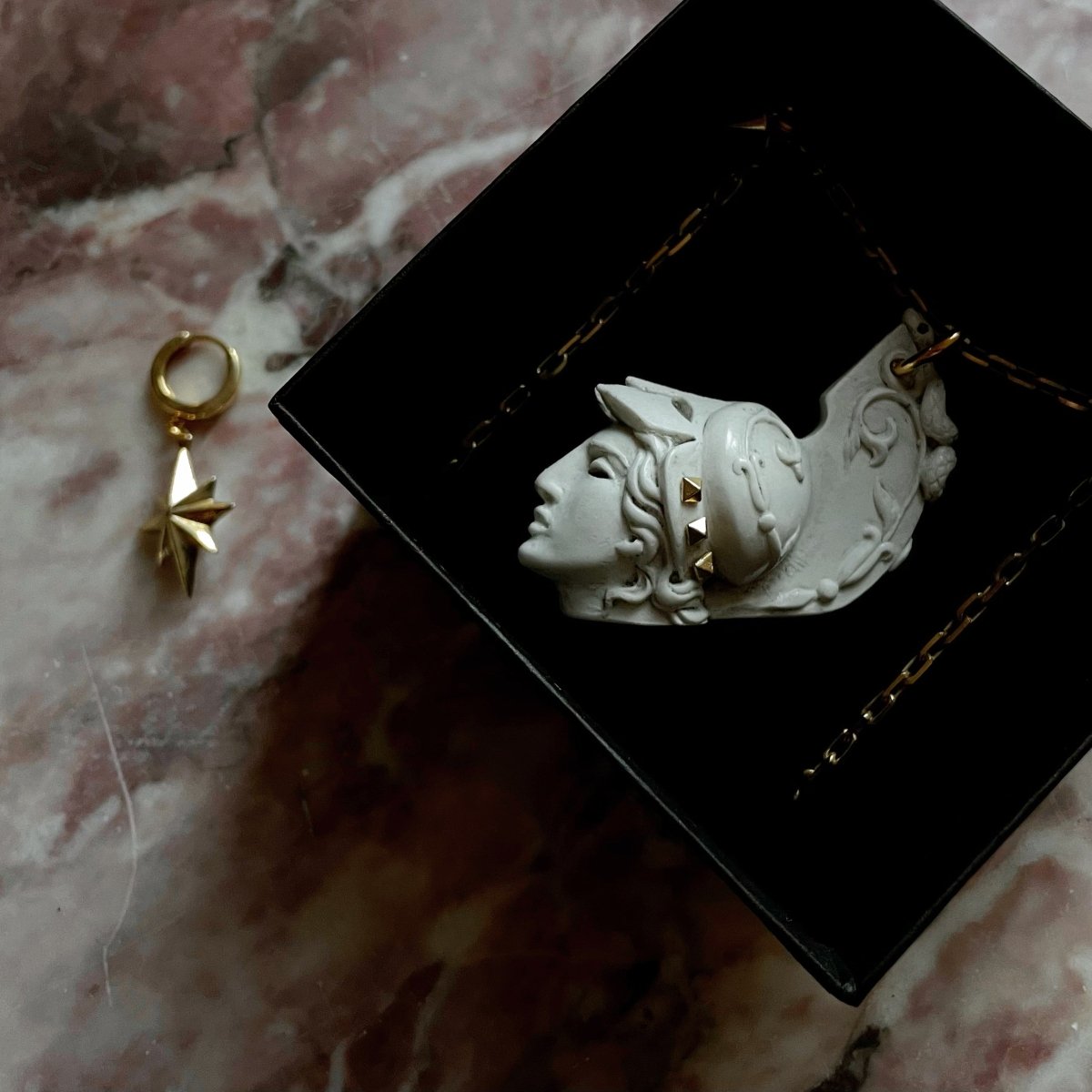 Athena pendant in a jewelry box next to the star earring by Macabre Gadgets on pink marble - lifestyle