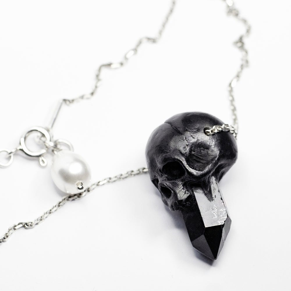 Crystal Skull pendant - black skull charm fixed on sterling silver chain on white surface