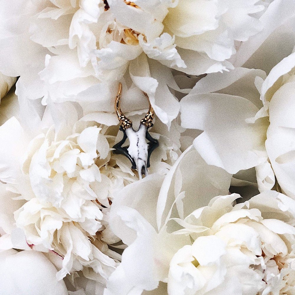 Doe Skull ring placed among a peony flower petals, surrounded by other peonies, gothic jewelry fashion editorial