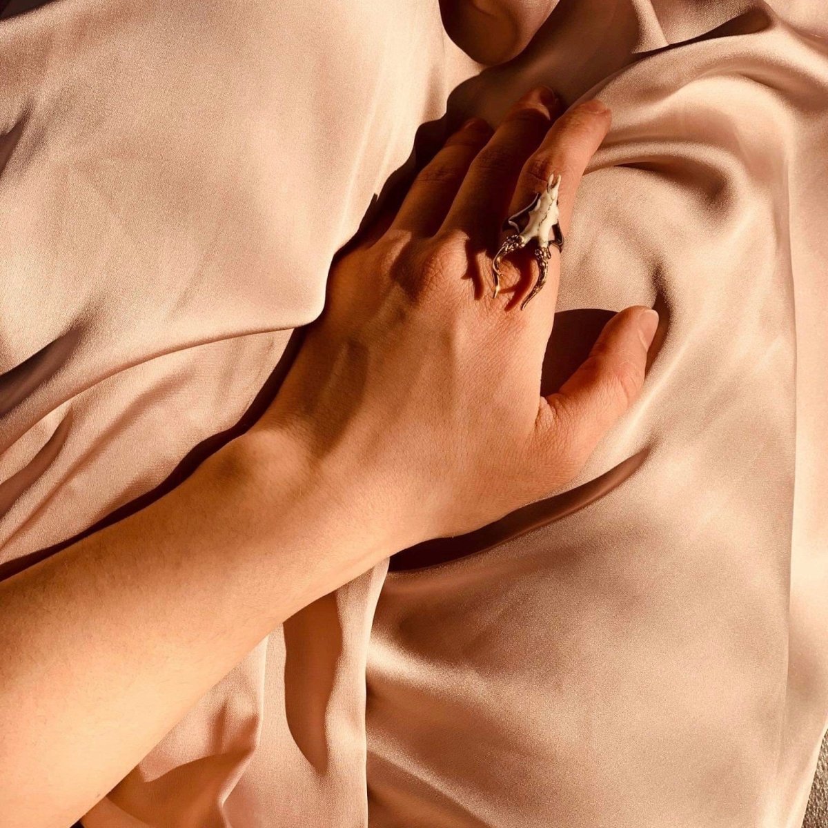 Doe Skull ring on a female model's hand, hand placed on a peachy silk creates elegant folds