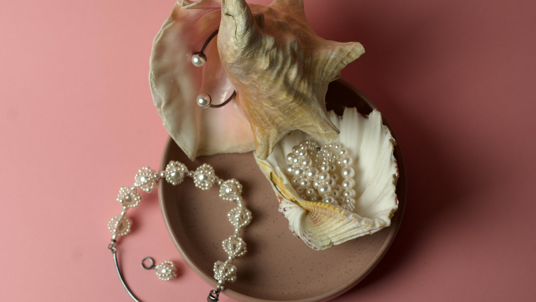 Pearl Jewelry by Macabre Gadgets: layered necklaces, pearl chokers and silver bracelets are displayed on a huge seashells on a pink background