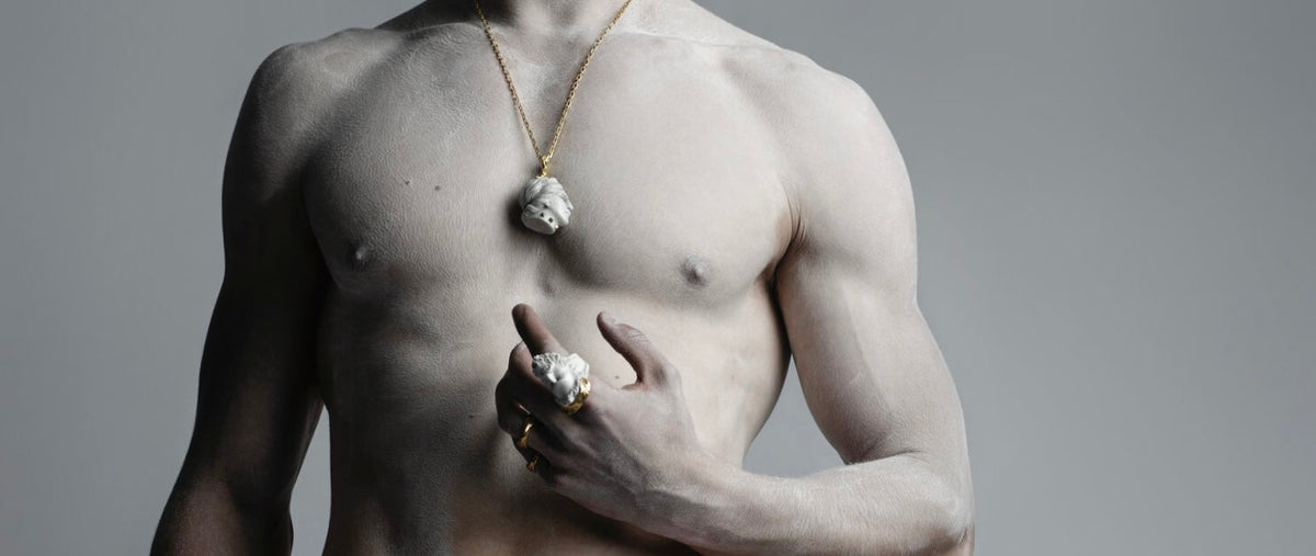 The image representing a blog post showing a bare chested  torso male model generously covered in white powder to resemble marble sculpture and wearing Macabre Gadgets jewelry