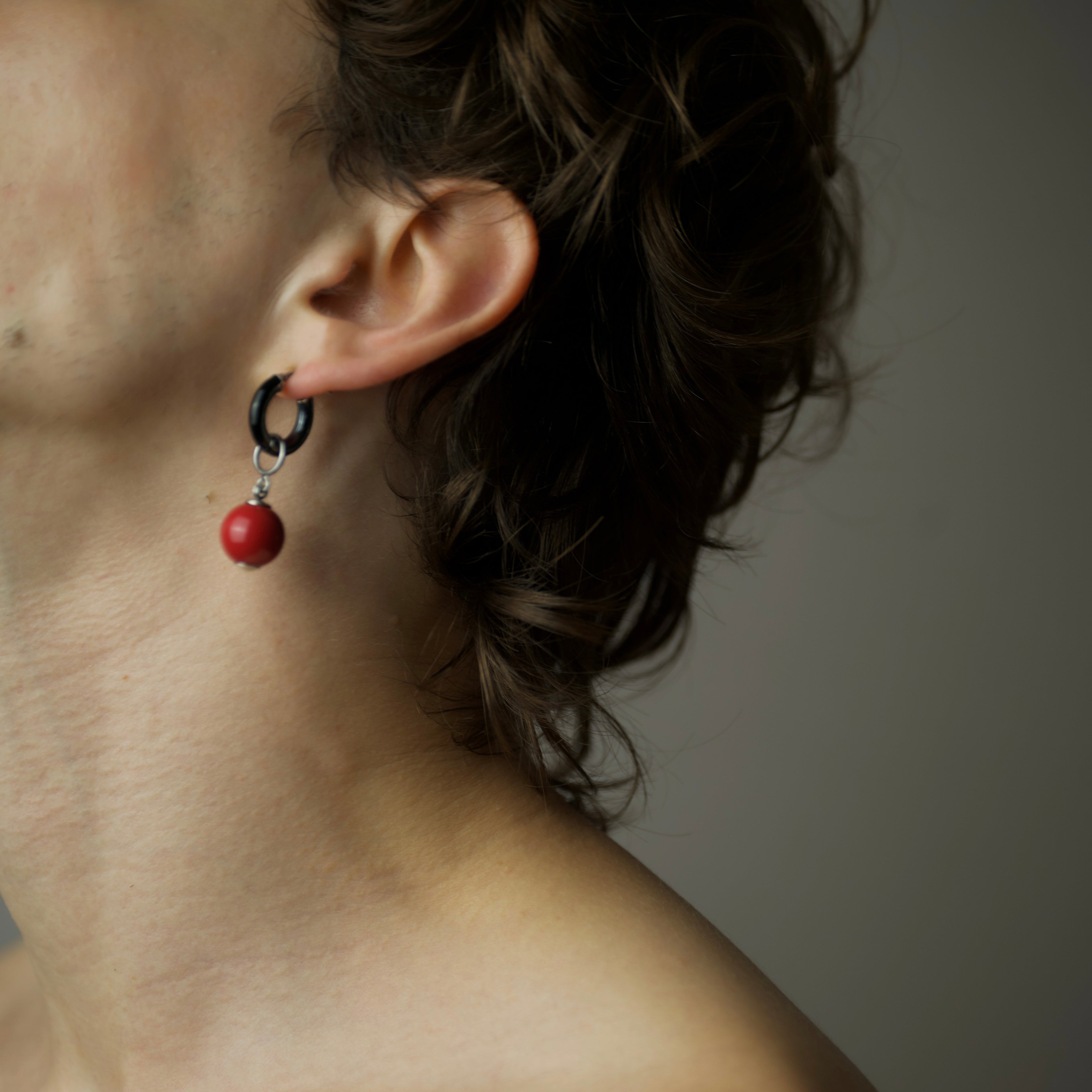 Close-up of an ear with a red bead earring against a neutral background