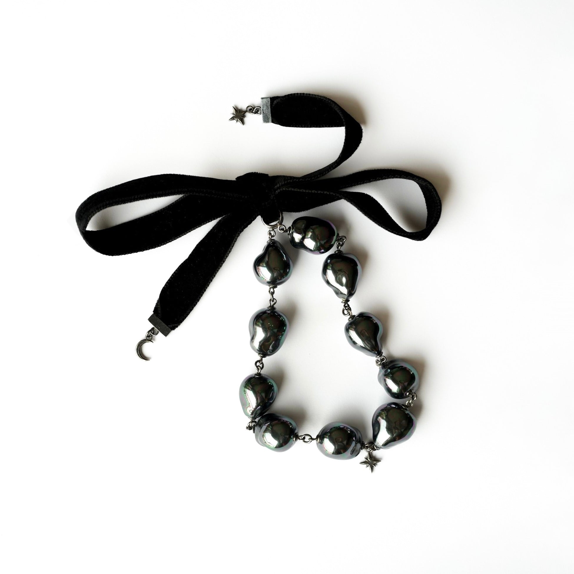 Black choker necklace with large black pearls and a small star pendant and a black velvet  ribbon on a white background