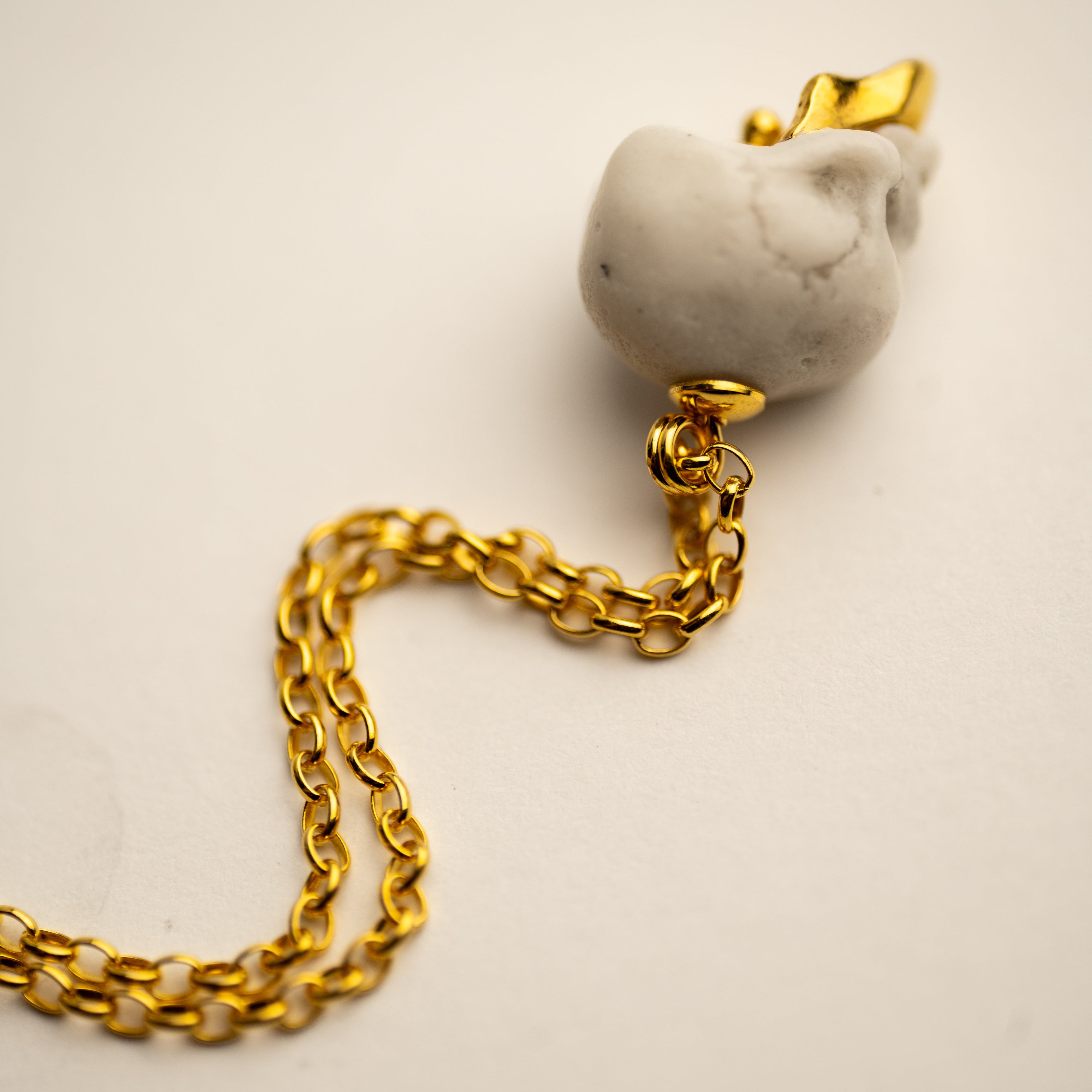 Gold chain with a white marble Ancient Skull pendant on a beige background