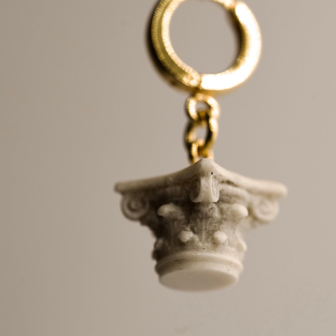 Corinth charm resembling an architectural column on a hoop earring against plain background