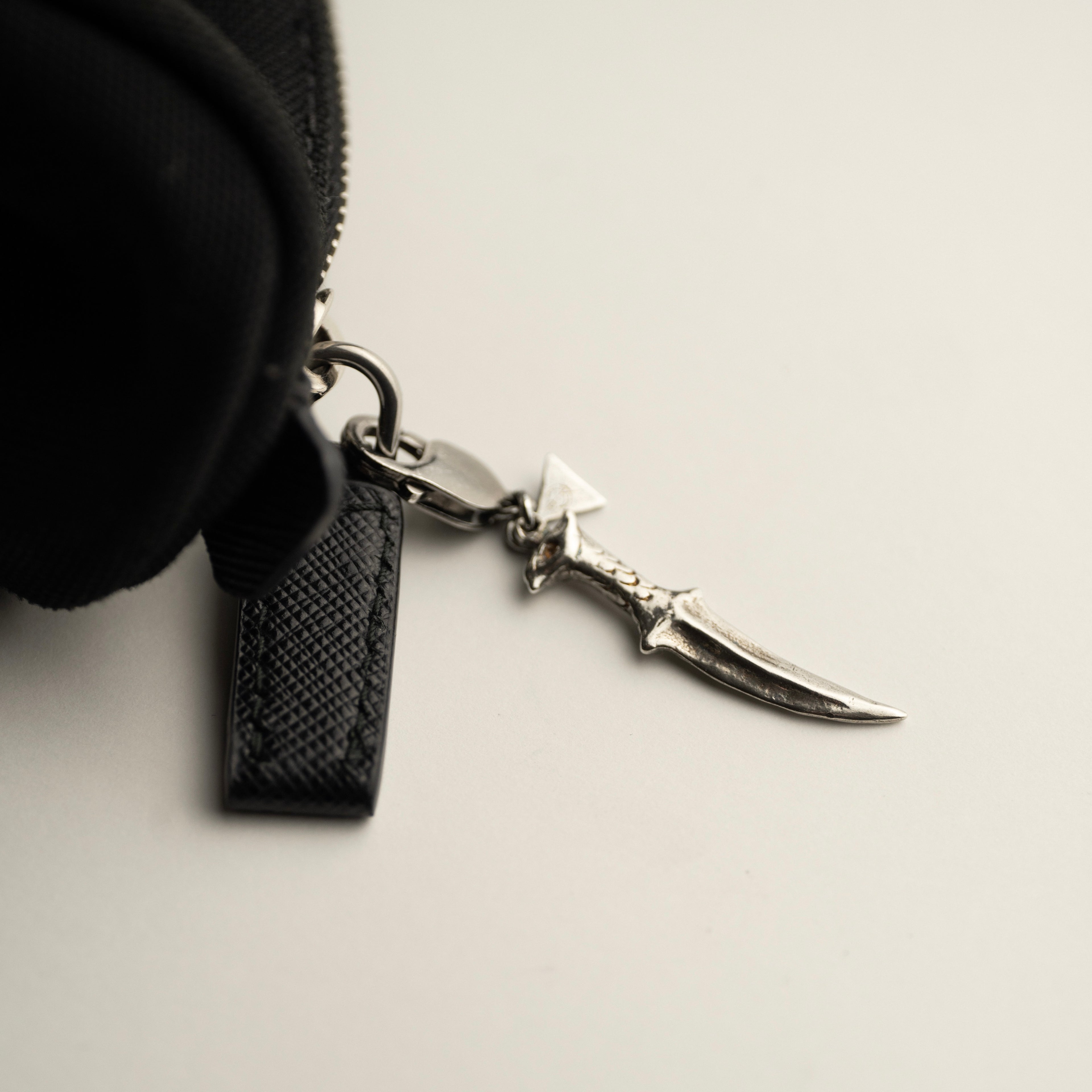 Black pouch with a silver dagger-shaped keychain on a light gray background