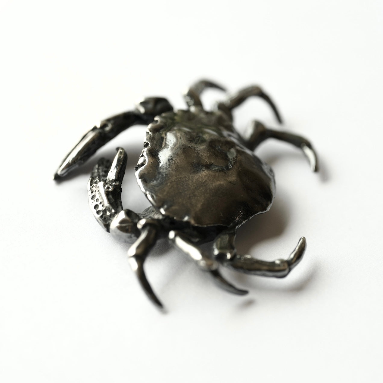 Metallic black and shiny crab-shaped brooch on a white background