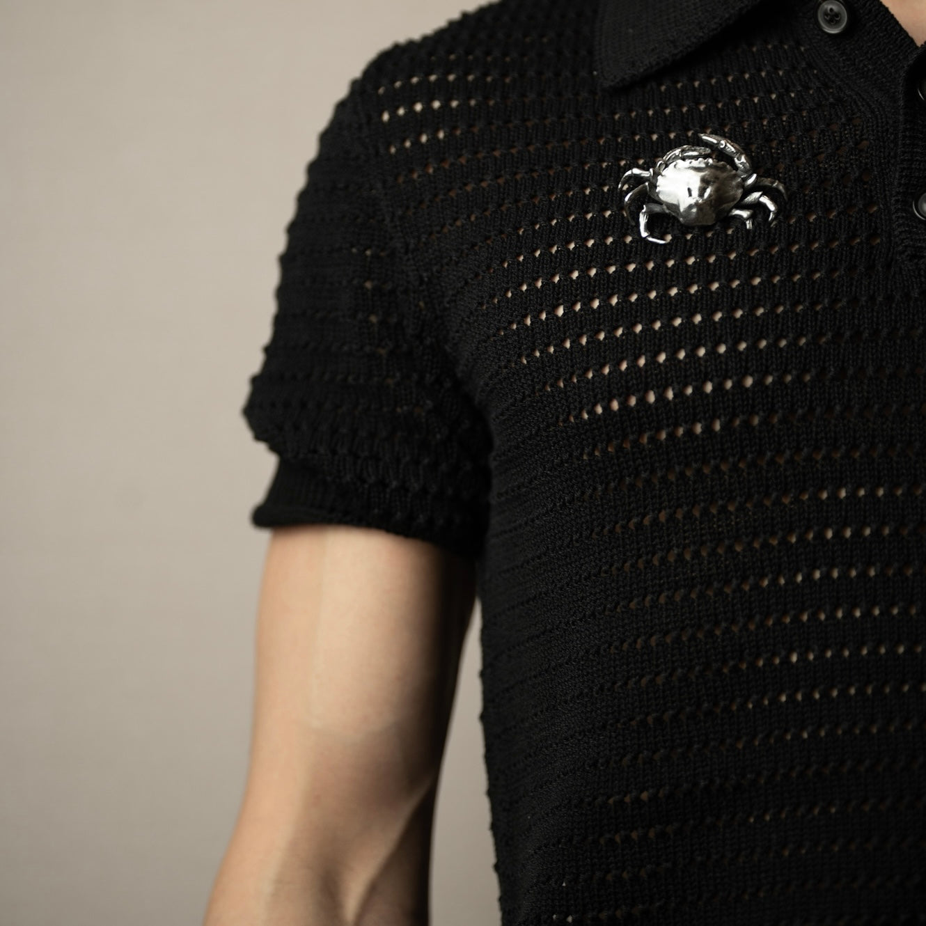 A man in black seeater wearing a silver crab brooch on a neutral background