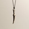 Griffin Sabre pendant - silver dagger-shaped pendant on a chain against a beige background
