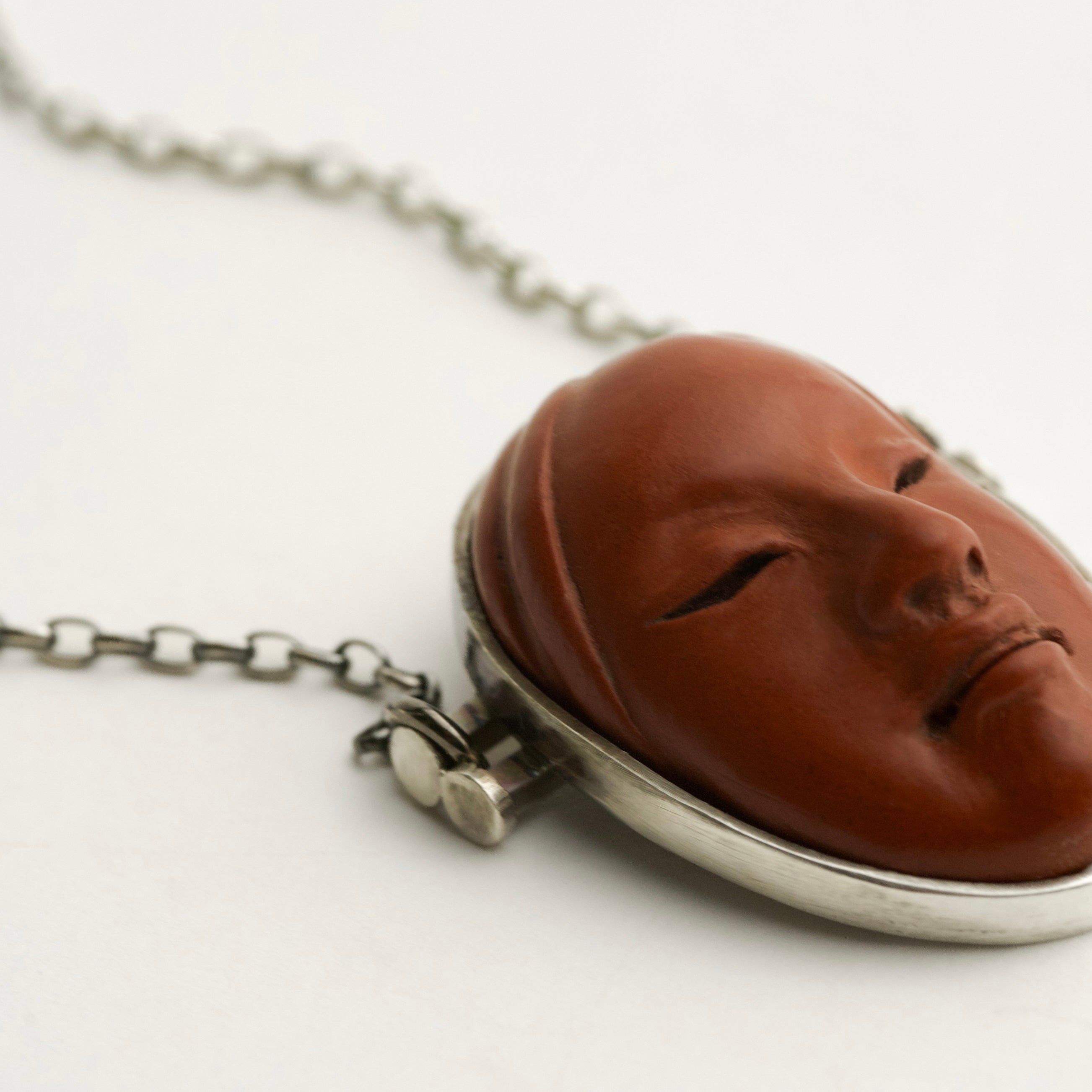 Necklace with a Noh mask-shaped pendant in sterling silver and terracotta on a white background