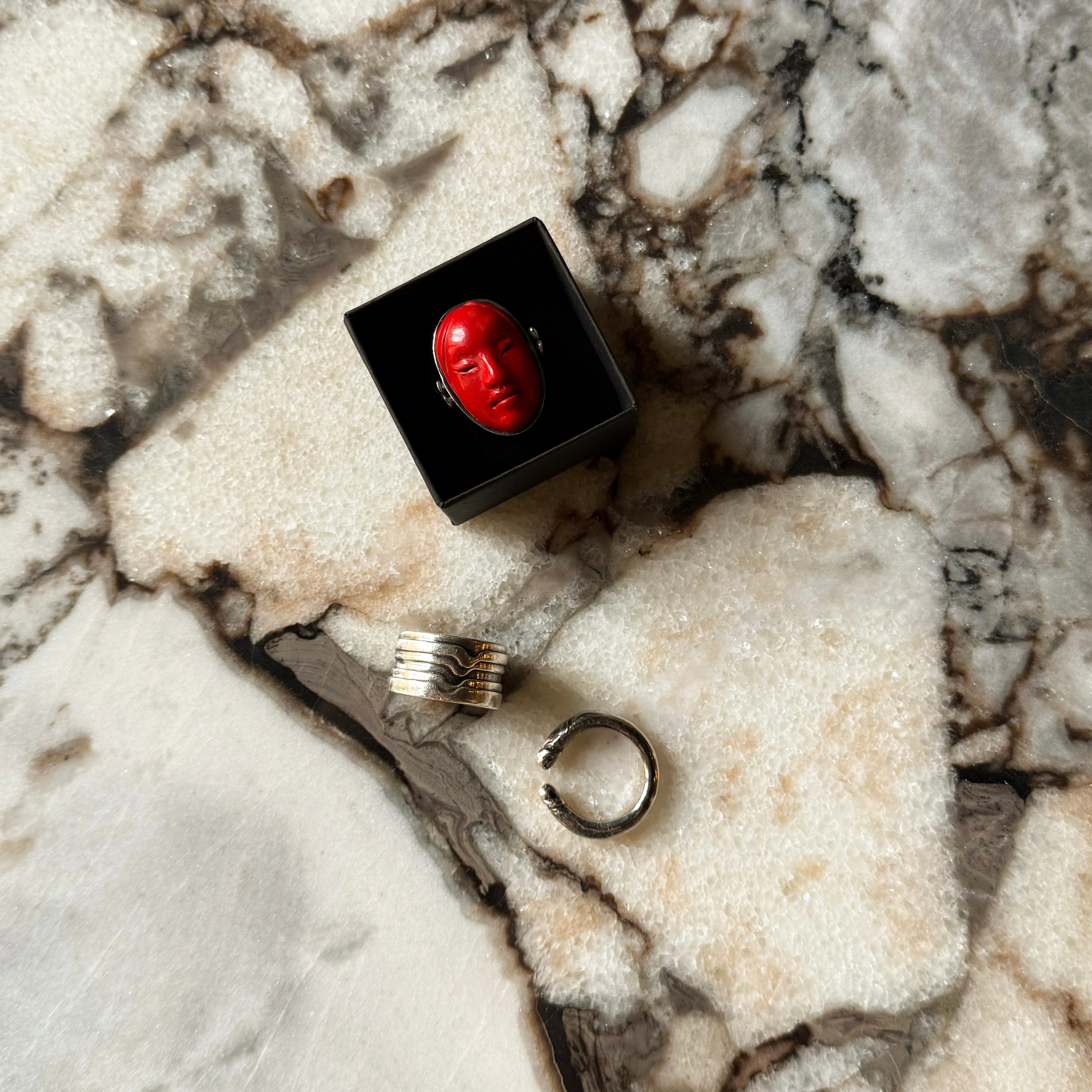 Lifestyle shot of a Mask ring in red color in a black box on a marble surface
