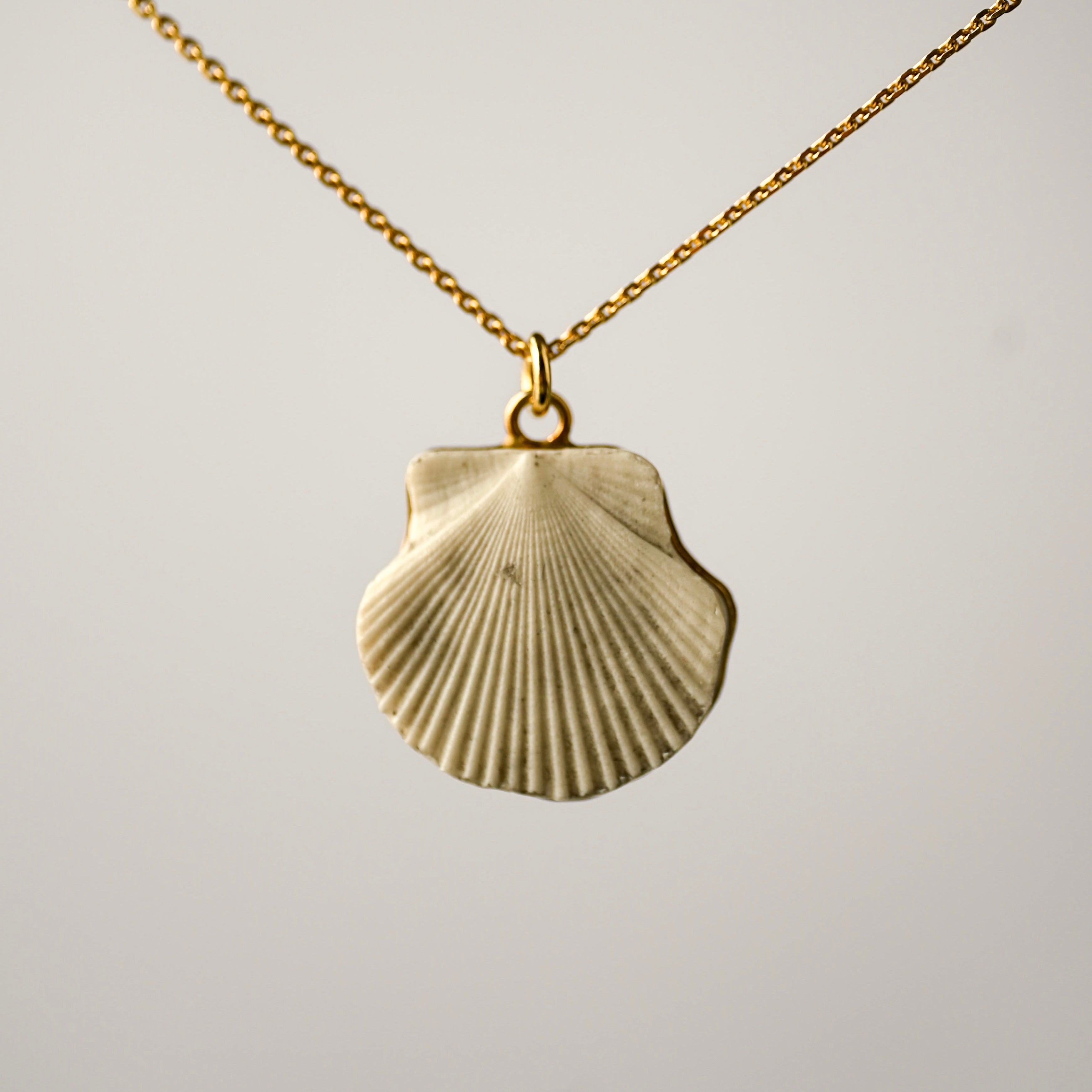Marble and gold shell shaped pendant necklace hand crafted by Macabre Gadgets on light grey background, front view showing the fixture to the chain.