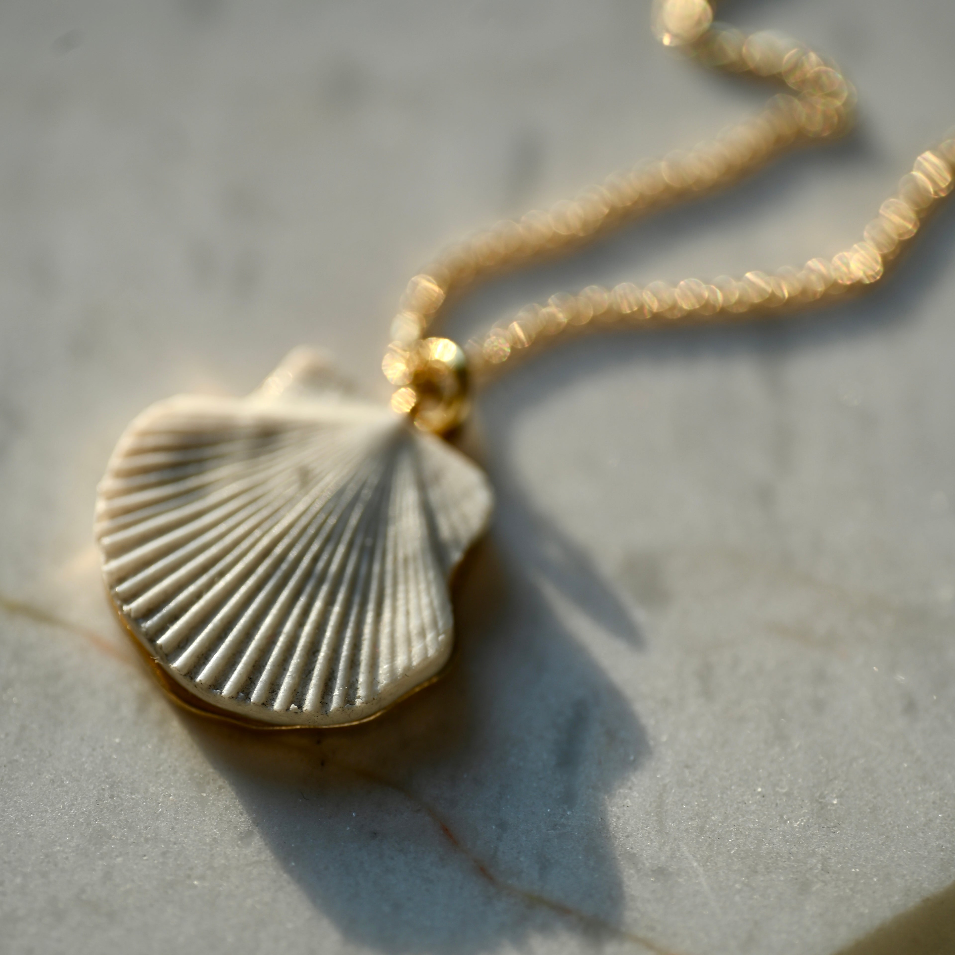 Sea Shell pendant (24K gold plated variant) on a white marble surface, close up of the shell.