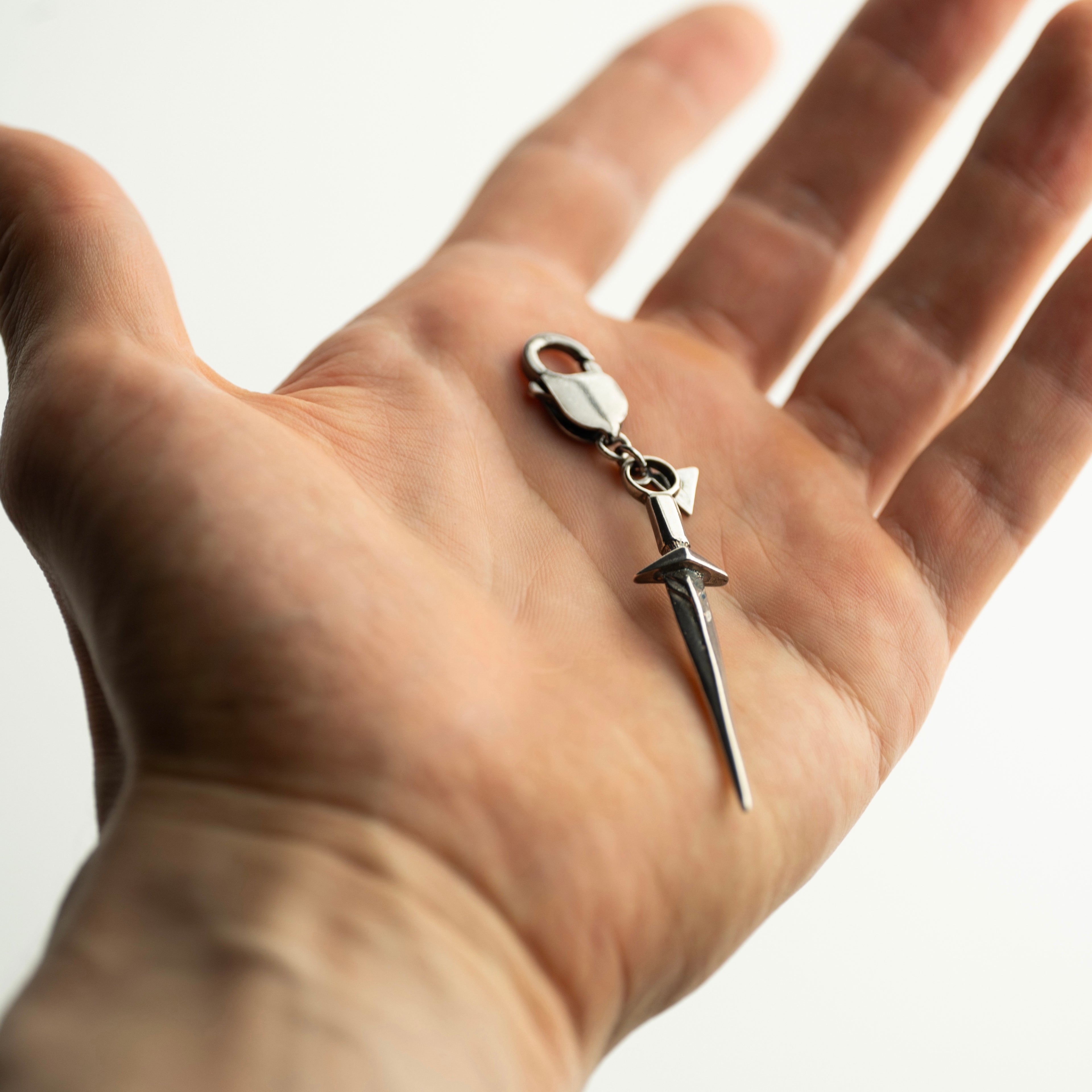 Sterling silver Sword charm handcrafted by Macabre Gadgets in a hand - a size comparison shot