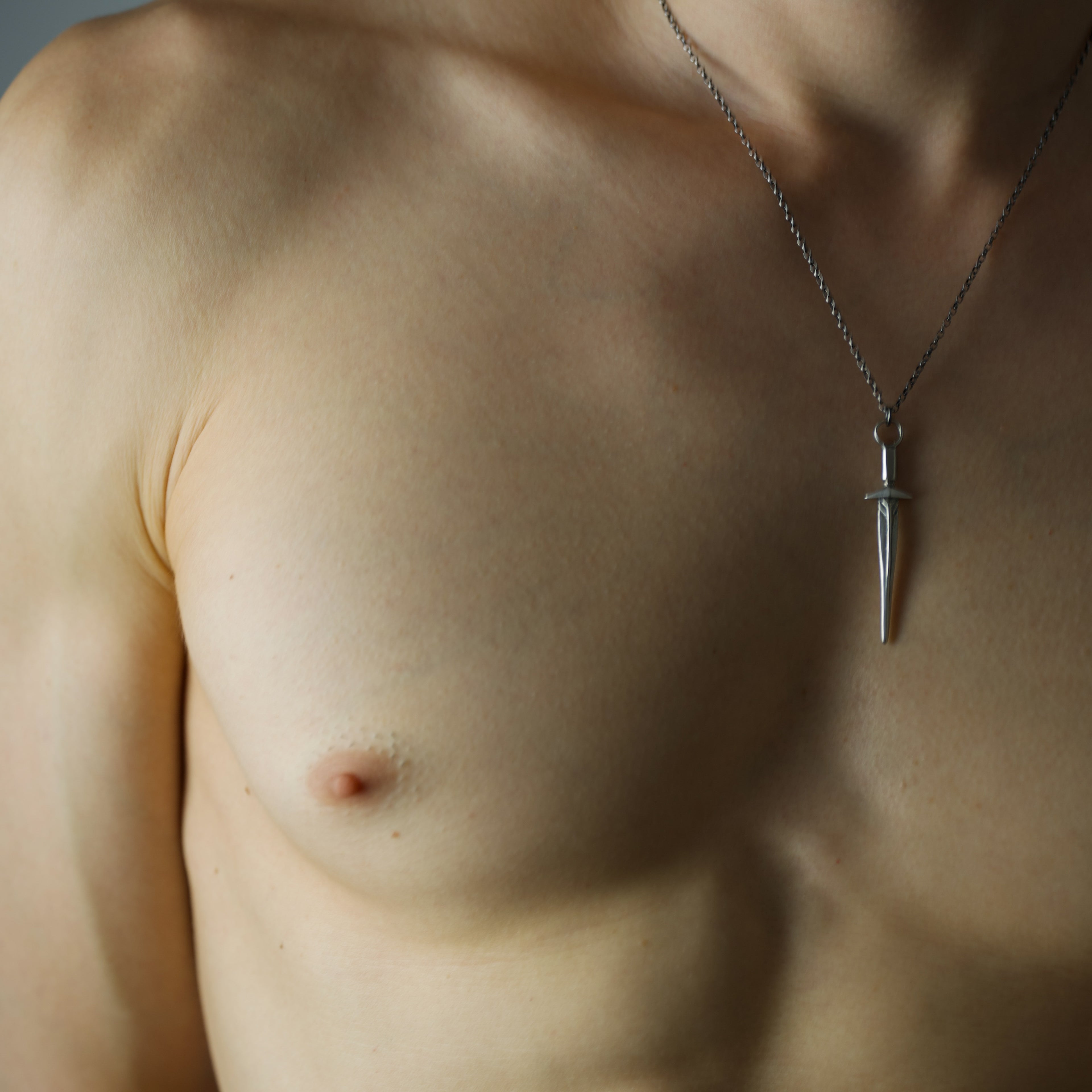 Sword pendant - close-up of a person wearing a sword-shaped necklace with a pendant on a neutral background
