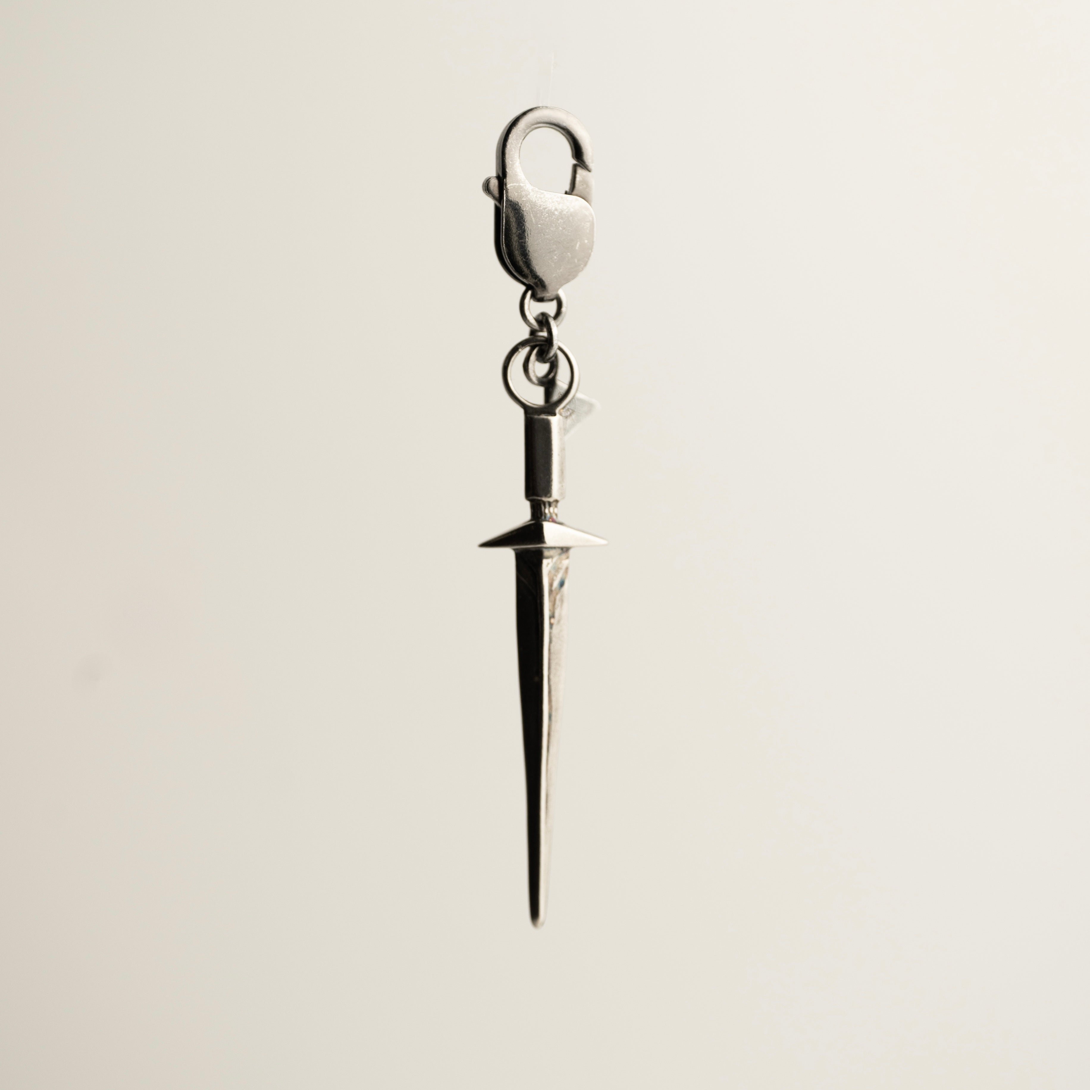 Silver dagger-shaped charm on a beige background - Sword keychain charm by Macabre Gadgets