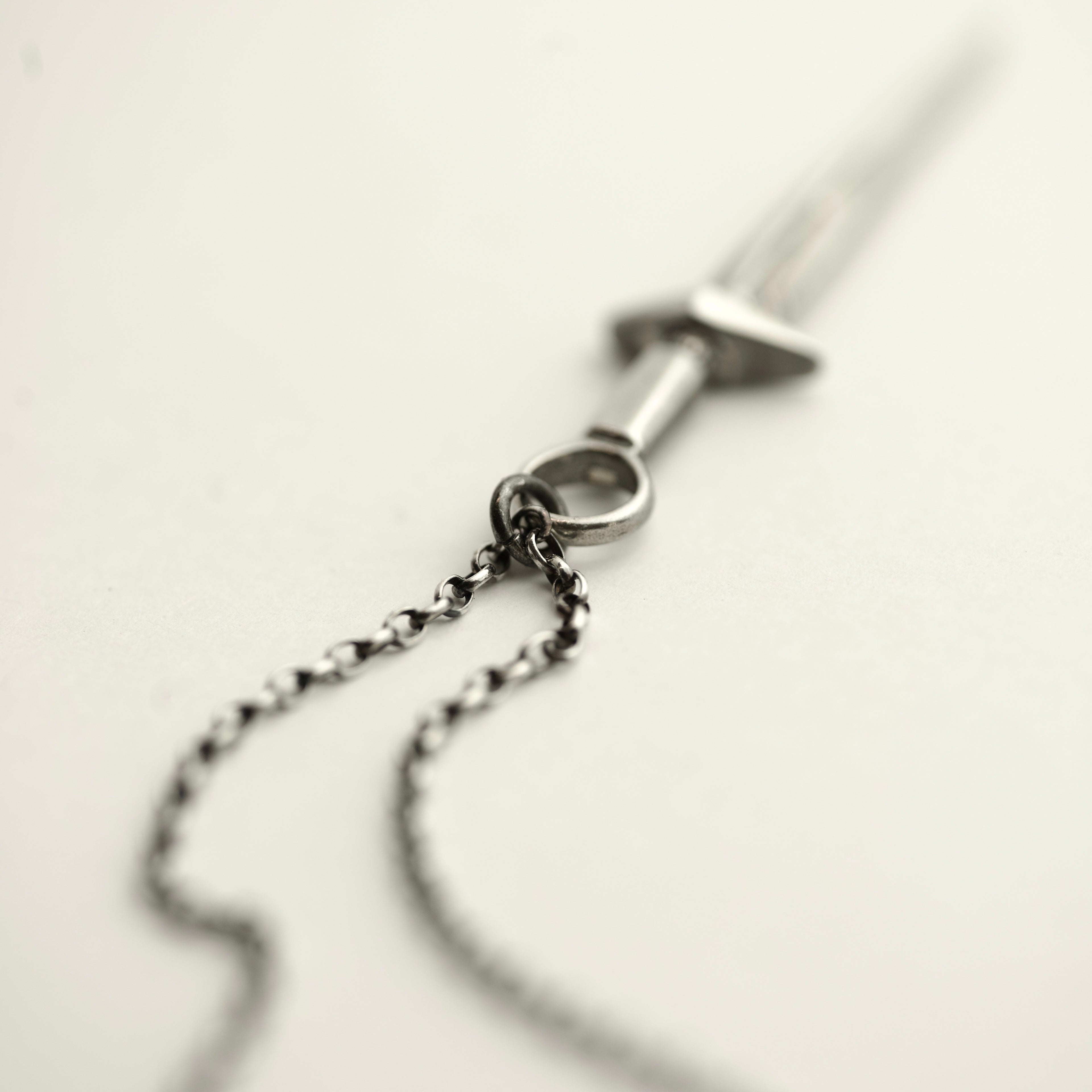 Close-up of a silver chain necklace with a sword pendant on a light background
