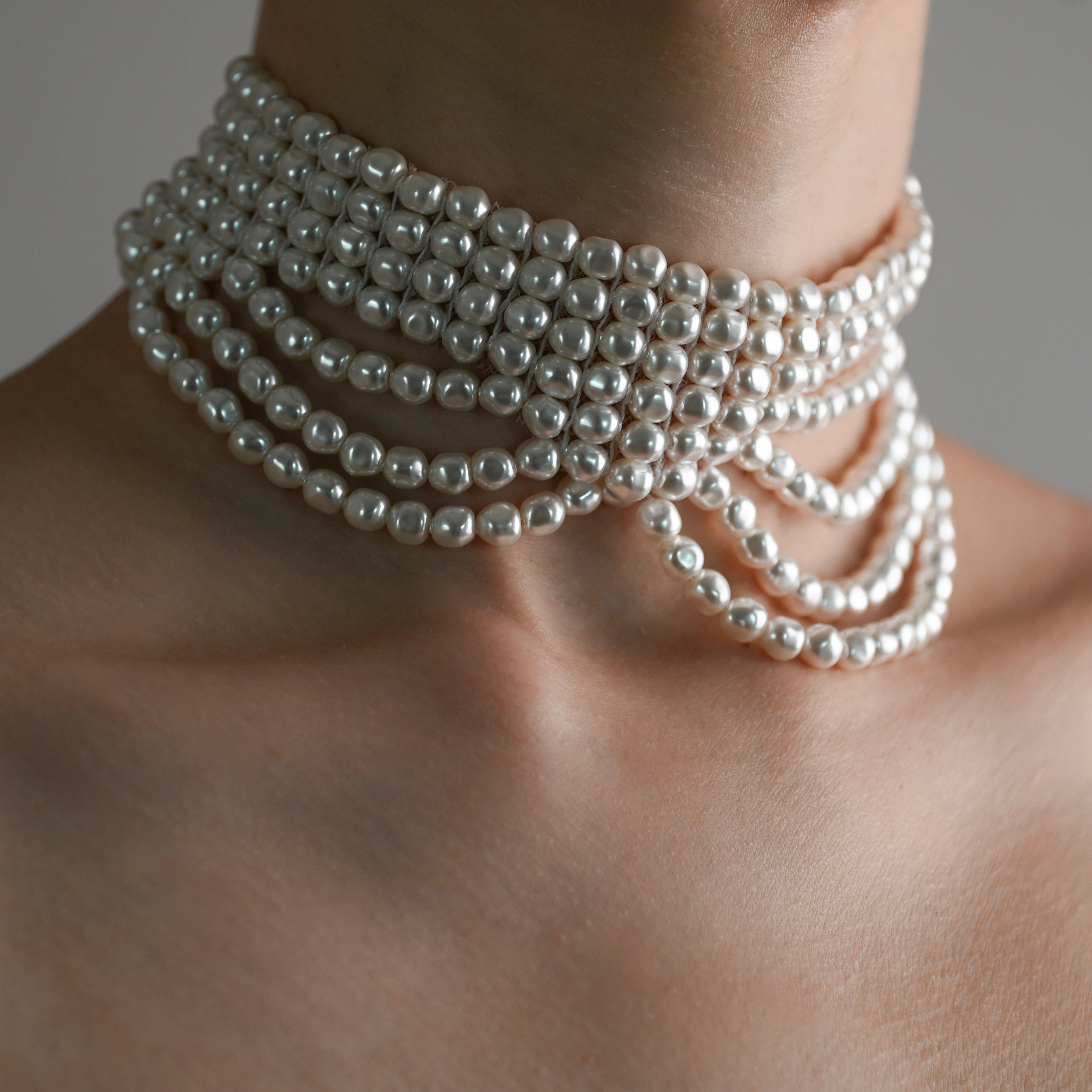 Multi layered pearl chocker on a person's neck against a neutral background