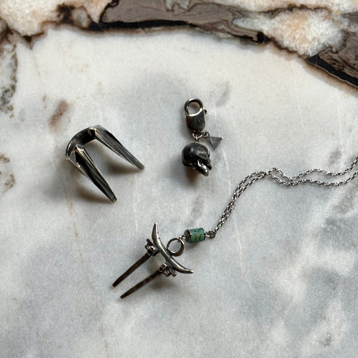 Marble skull charm — black marble with sterling silver jaw on grey marble surface alongside Mantis ring and Moonglade Gate pendant