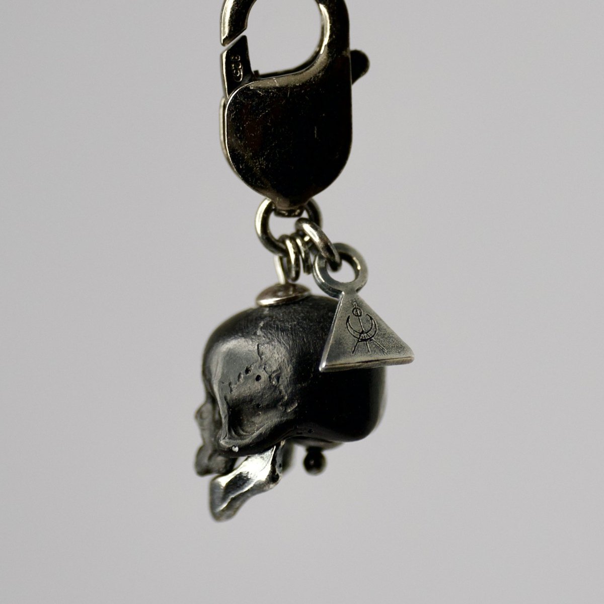 Marble skull charm — black marble with sterling silver jaw, profile view on grey surface
