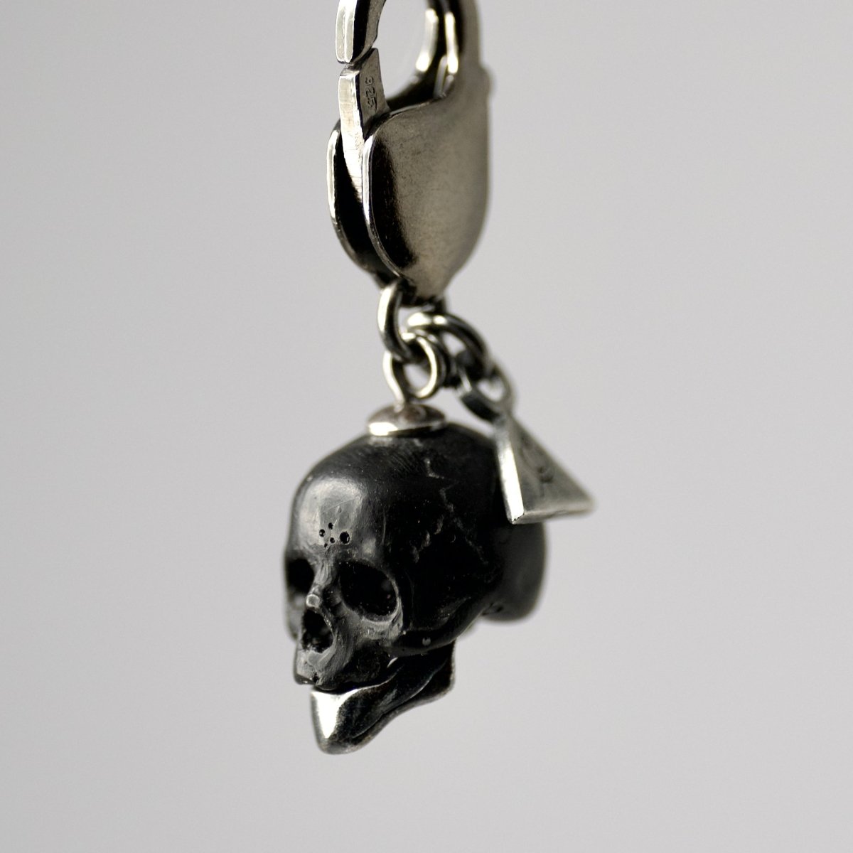 Marble skull charm — black marble with sterling silver jaw, three-quarter view on grey surface