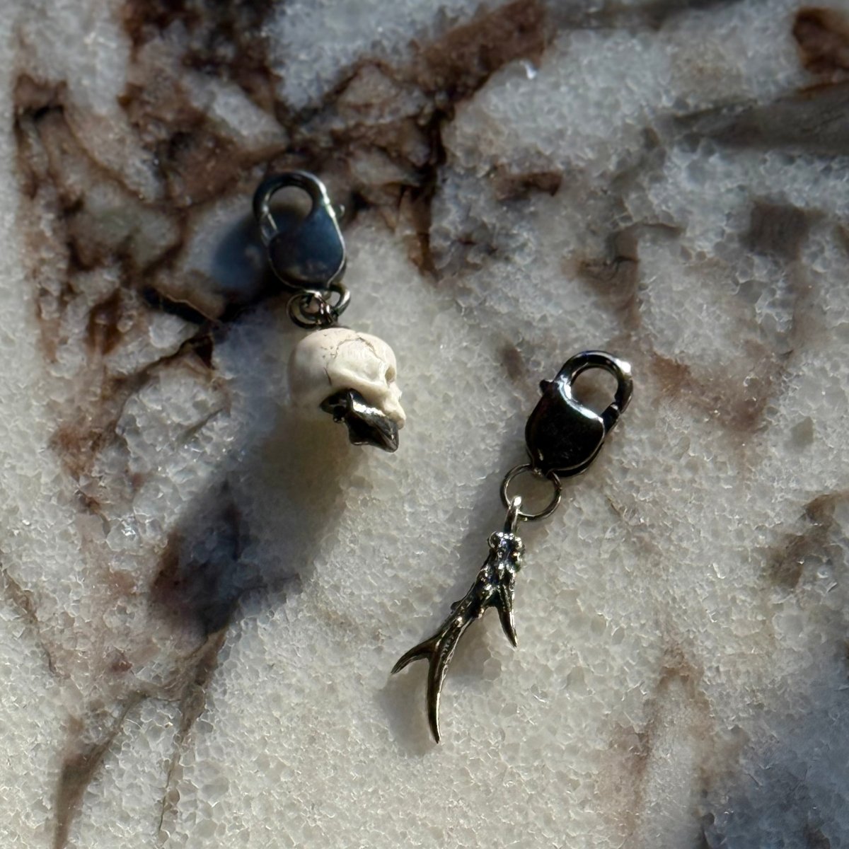 Marble skull charm — white marble with sterling silver jaw alongside horn charm on marble surface