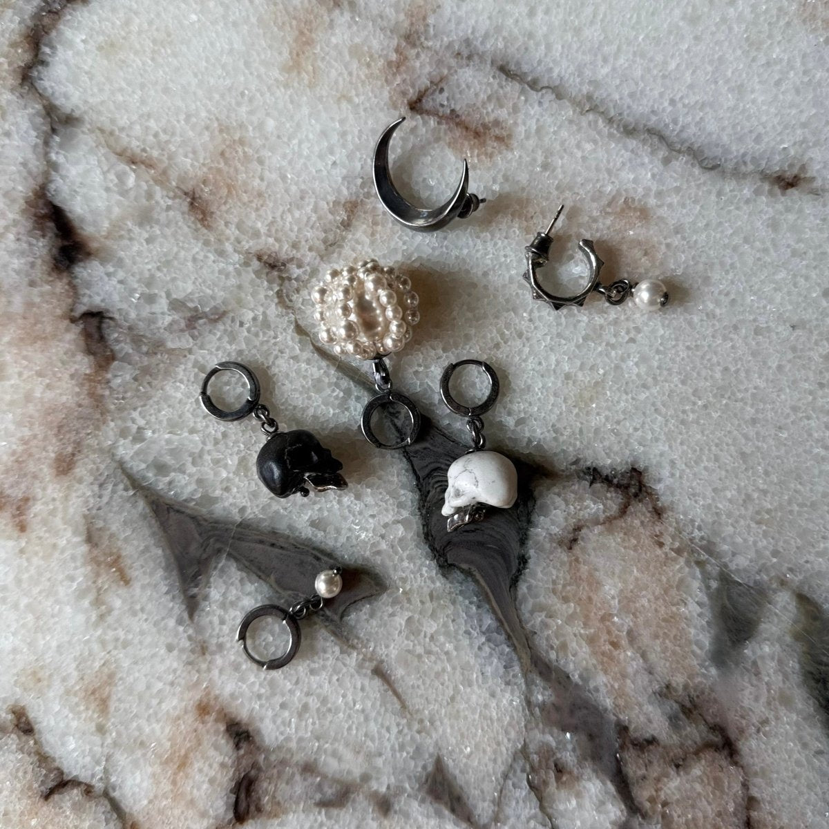 Luna earring with Ancient Skull earring and  other different earrings on a marble surface