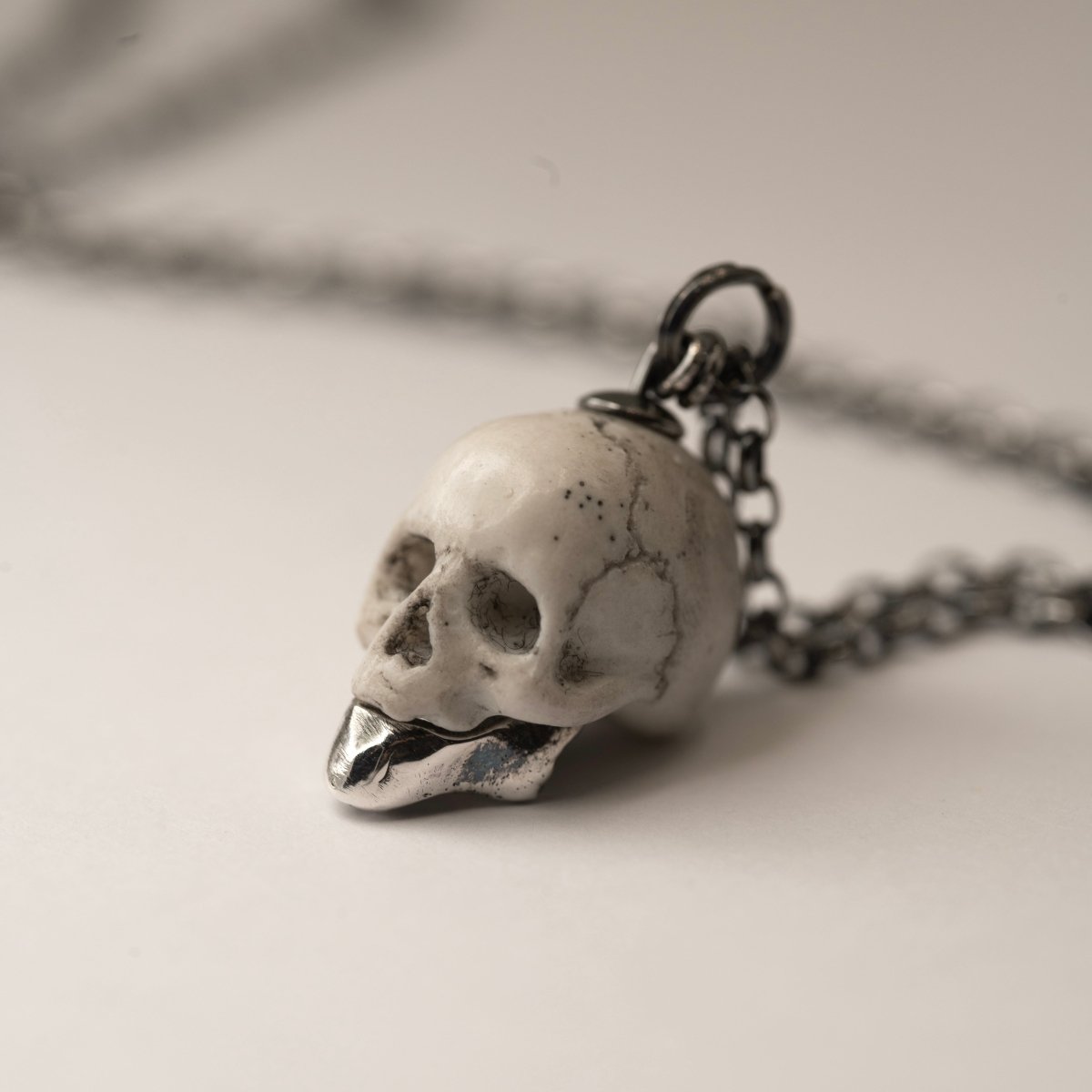 Ancient Skull pendant by Macabre Gadgets on a light surface, close-up of the marble skull pendant with silver jaw