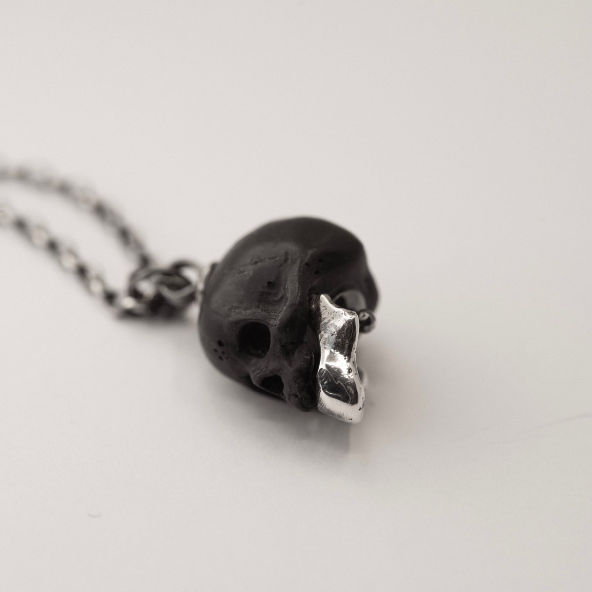 Ancient Skull pendant - black variant - placed on white surface, focus on skull pendant and its texture