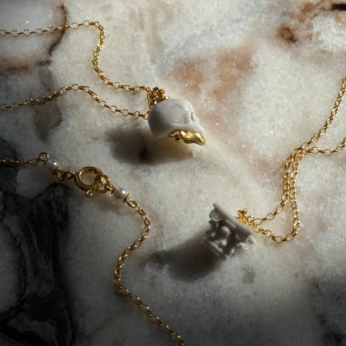 Ancient Skull pendant and Corinth pendant on white marble surface — Macabre Gadgets skull jewelry