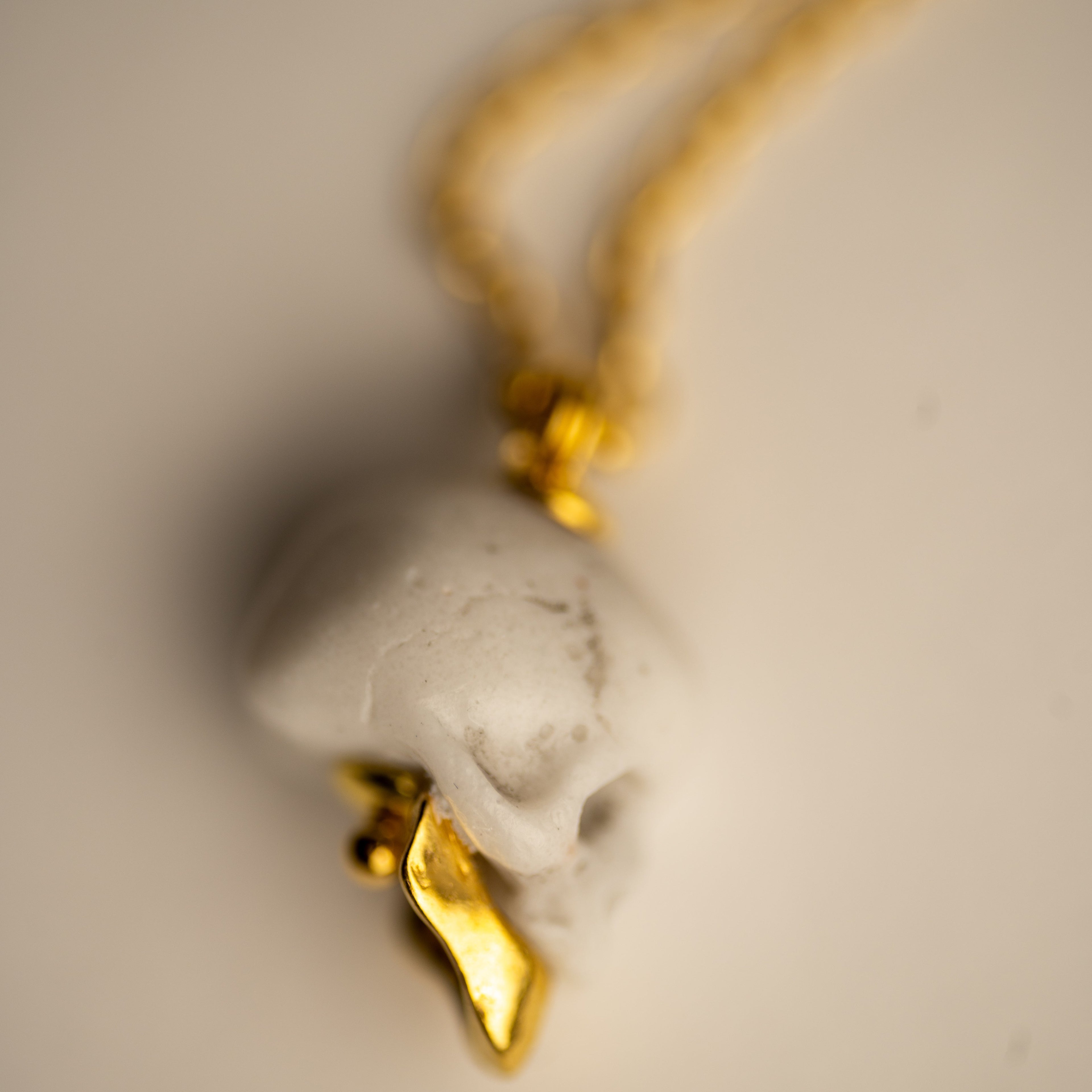 Miniature marble skull pendant close-up — white marble with gold-plated sterling silver jaw on chain