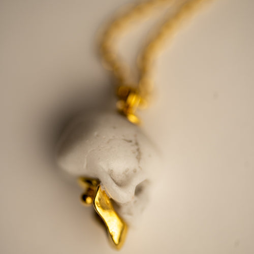 Miniature marble skull pendant close-up — white marble with gold-plated sterling silver jaw on chain