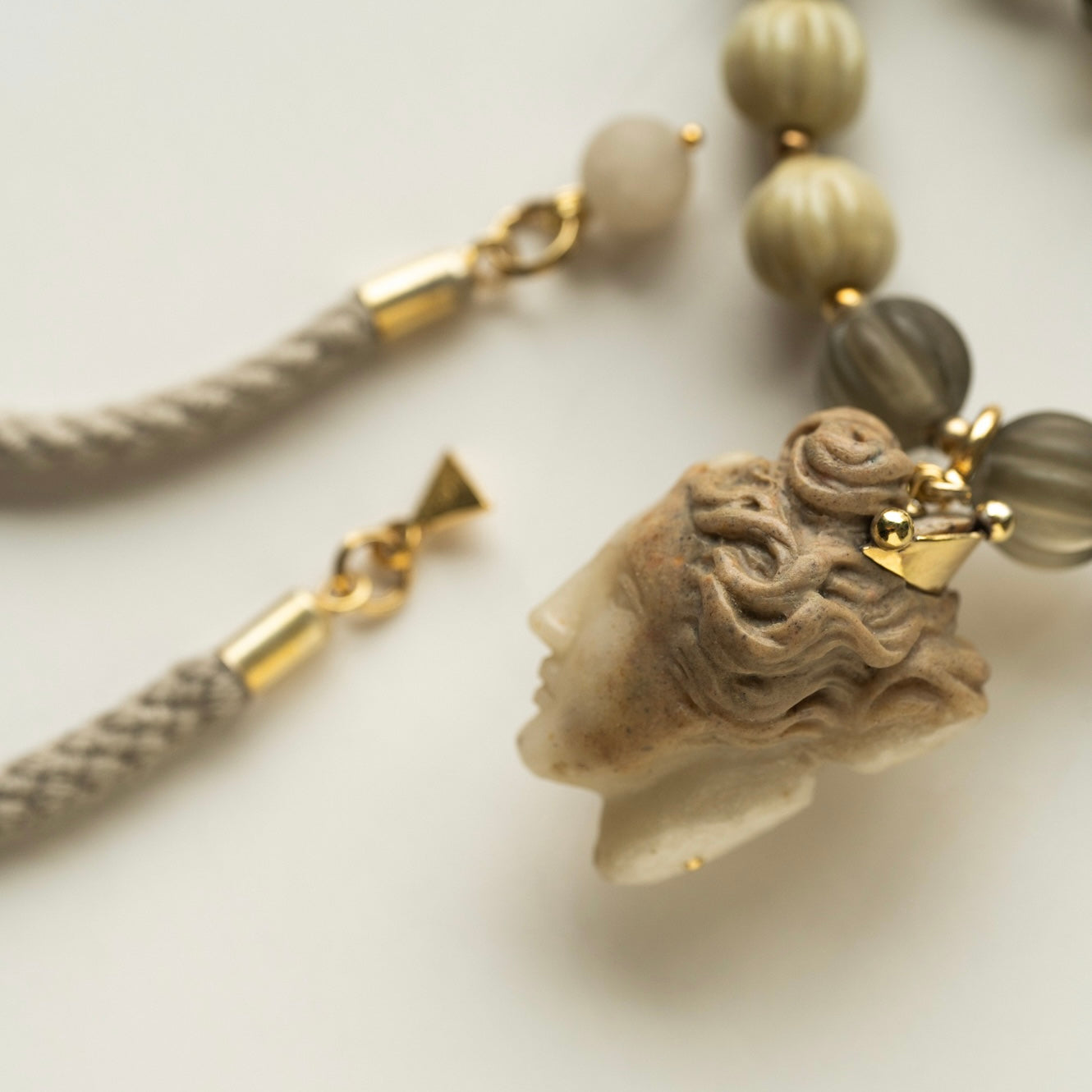 Necklace with a marble stone pendant - head of a Ancient Greek goddess with a golden crown and braided cord on a light background