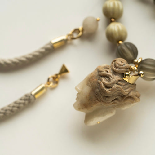 Necklace with a marble stone pendant - head of a Ancient Greek goddess with a golden crown and braided cord on a light background