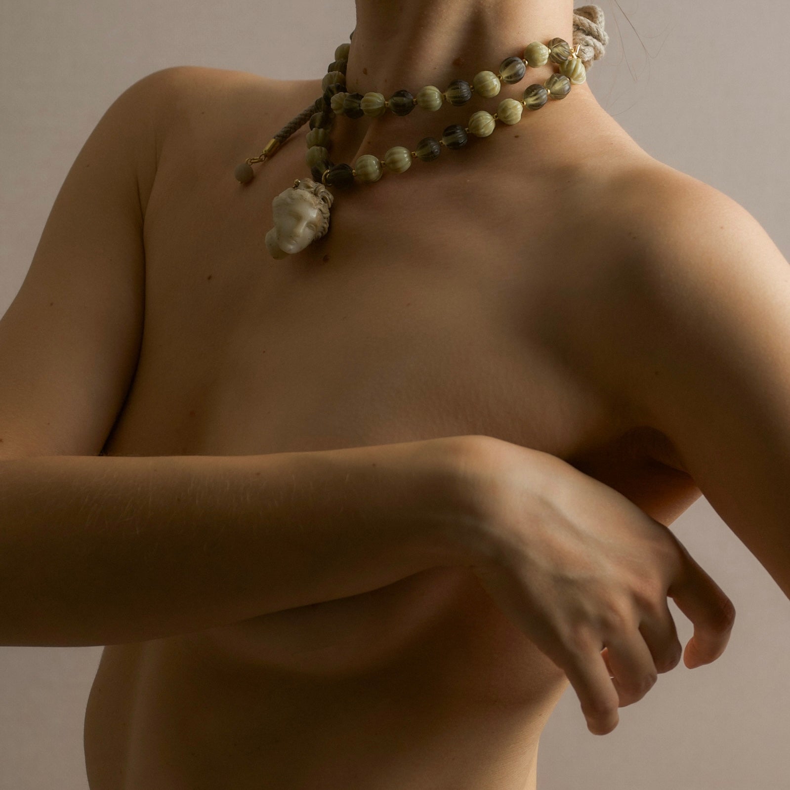 Female model wearing a beaded Aphrodite necklace on a neutral background - editorial shot echoing ancient sculpture of Venus