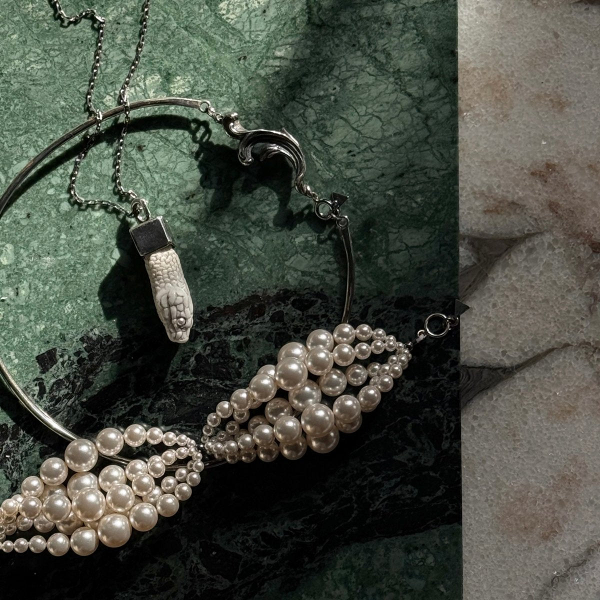 Aspis pendant with other jewelry on a green marble surface