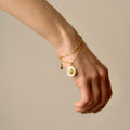 Aster bracelet - gold variant - on a female model's hand, layered chains and coin charm are clearly visible