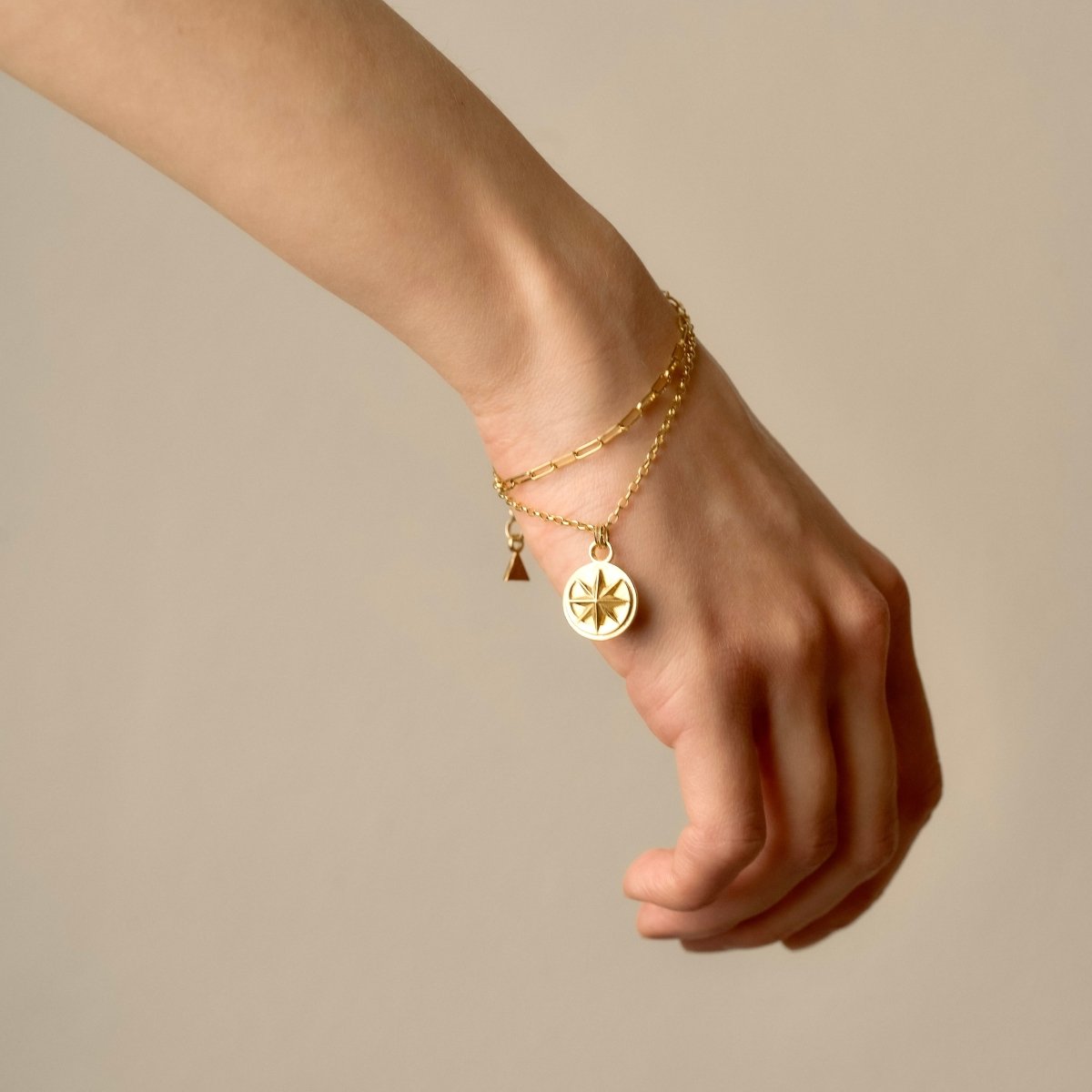 Aster bracelet - gold variant - on a female model's hand, layered chains and coin charm are clearly visible