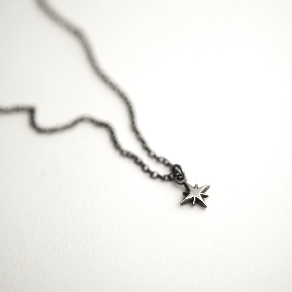 Asteria Silver Star pendant placed on a white surface, with focus on the star pendant, while the chain is blurry