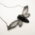 Cicada necklace - black variant - on a white surface, focus on the see-through wings