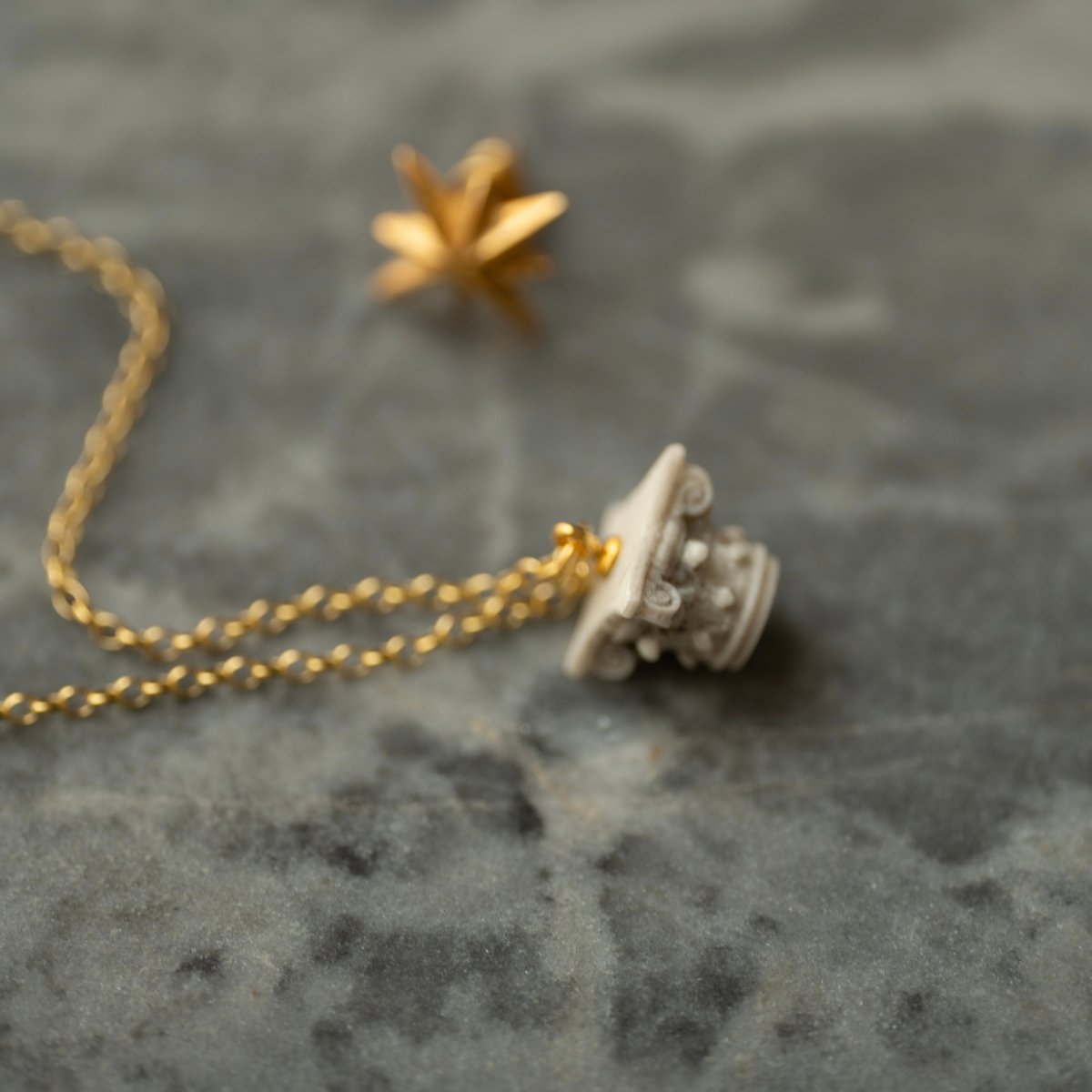 Corinth pendant placed on a marble surface next to the Star Stud earring