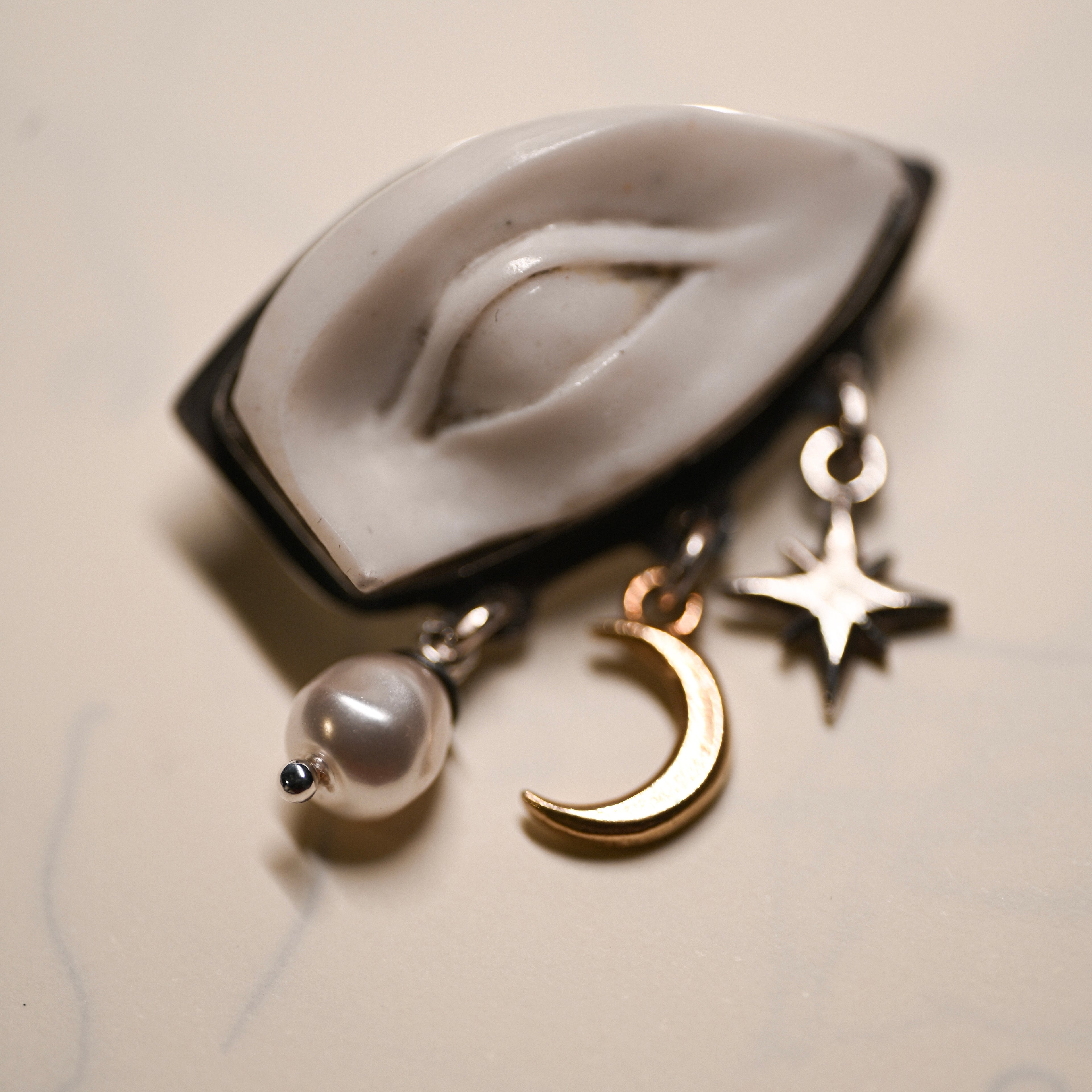 Close-up of white marble eye hand sculpted and set on a sterling silver brooch with moon, star and pearl charms on a light background