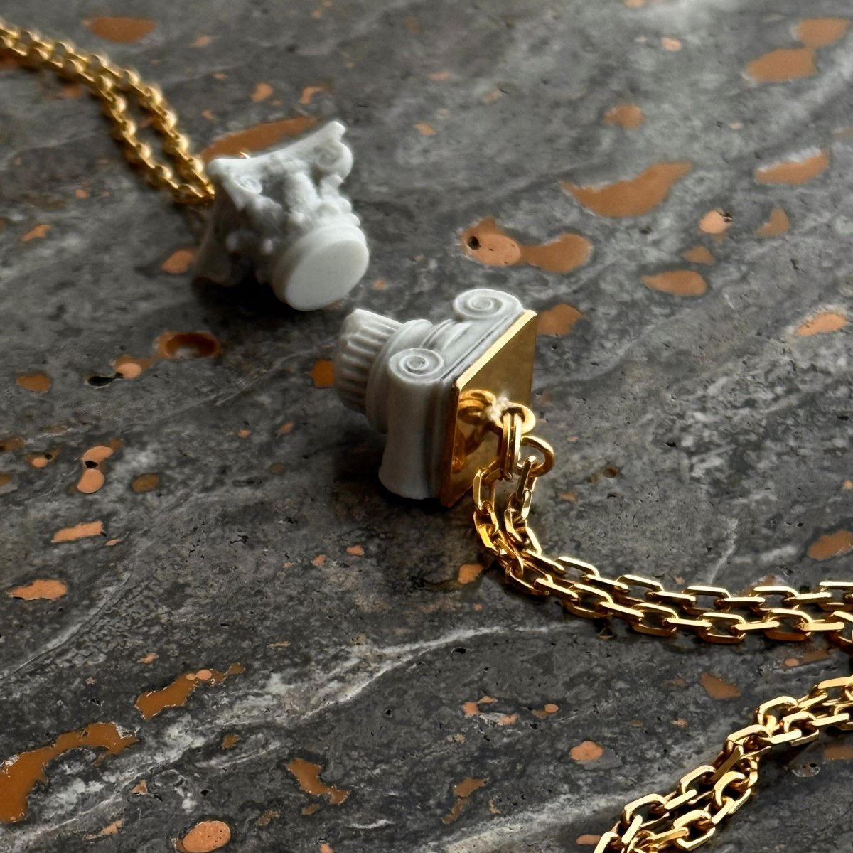 Ionic pendant and Corinth pendant on a black marble surface next to each other