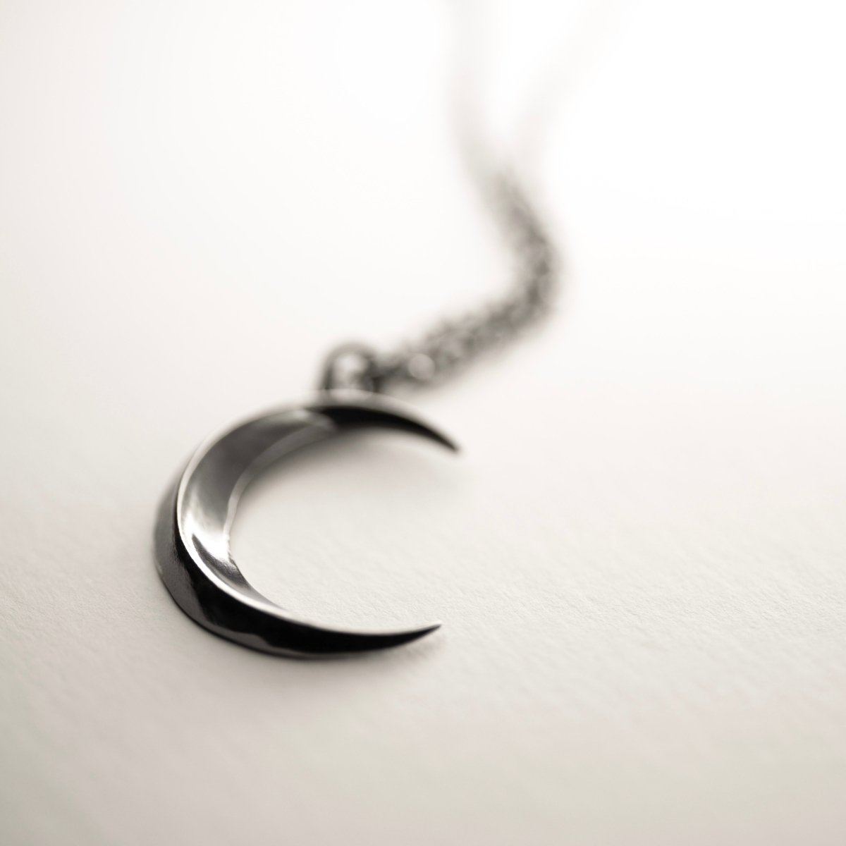Luna pendant on a white surface, focus only on the sleek moon, chain is blurry 