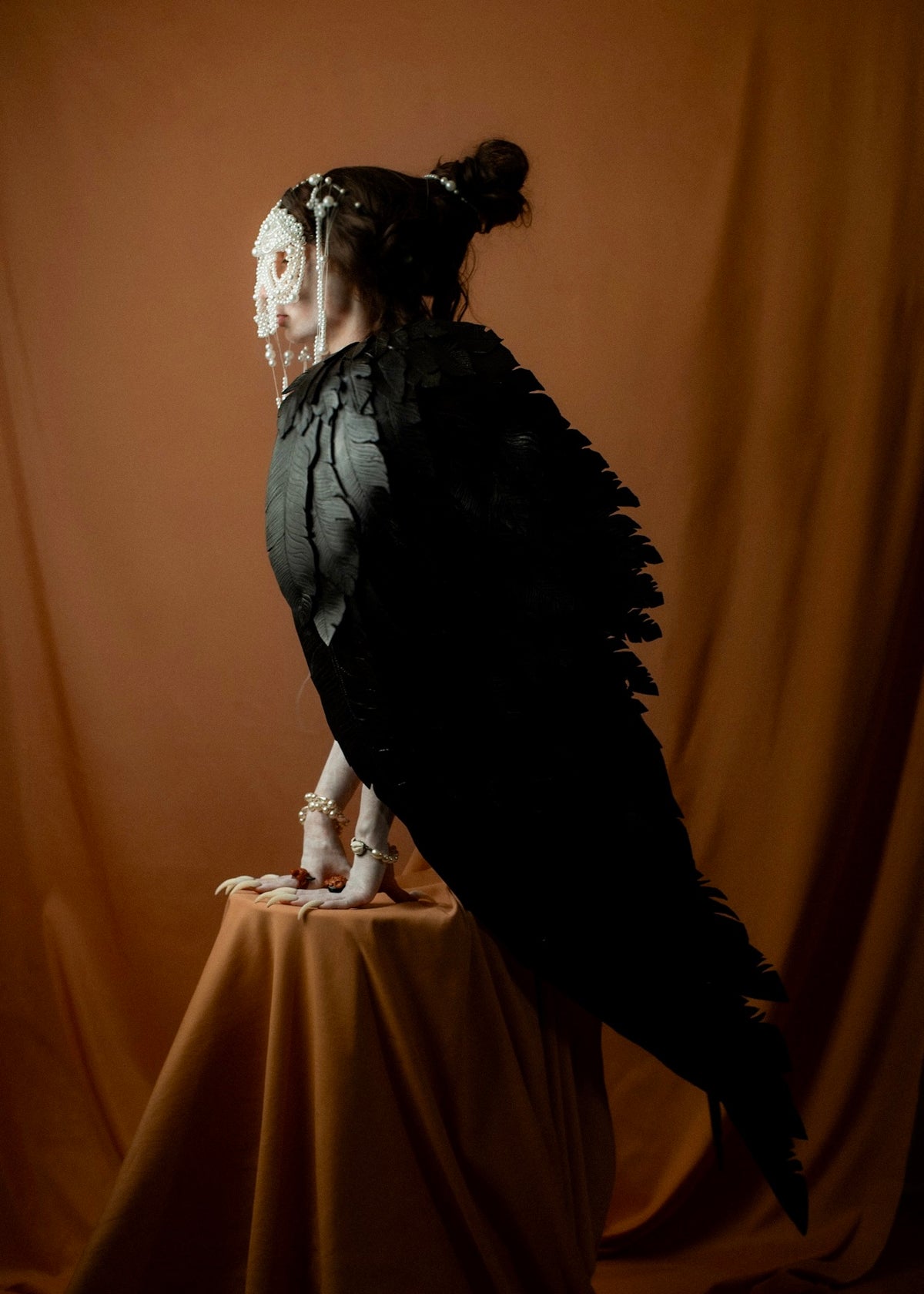 Ancient Greek Siren depicted as a black-feathered bird with a human head, seated on a pedestal against a terracotta background, Gods and Monsters THEA campaign | Macabre Gadgets