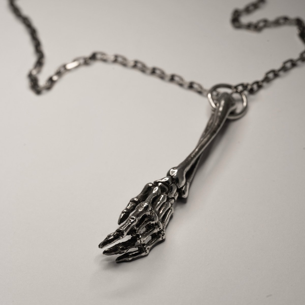 Silver Skeleton Arm pendant lying on a light surface, all details are clearly visible
